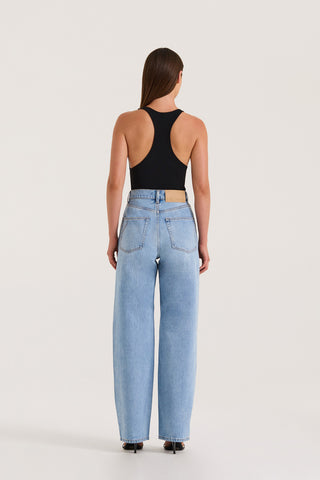 Back view of model wearing light wash straight-leg, high-rise petite jeans and a black tank top against a white background.