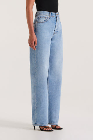 Close up view of model wearing light wash straight-leg, high-rise petite jeans against a white background.