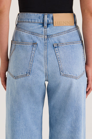 Close-up back view of a model wearing light wash petite jeans with a high-rise, straight-leg fit and a leather patch on the waistband against a white background.