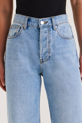 Close-up view of a model’s waistband in light wash jeans with a high-rise, straight-leg fit against a white background.
