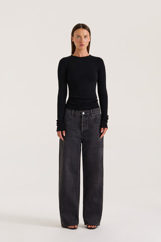 Petite model wearing a fitted black long-sleeve top and black jeans on a white background