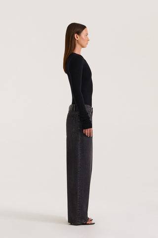 Side view of model wearing a black long-sleeve top and black wide leg jeans and fitted long sleeve black top on a white background