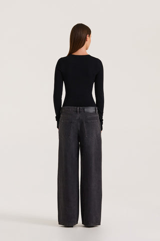 Back view of petite model wearing black wide leg jeans and a black long sleeve top on a white background