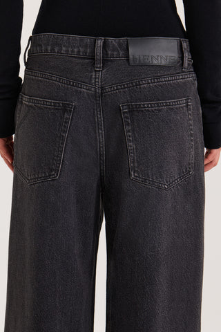Close up back view of model wearing black wide leg Jeans with a Henne leather patch on a white background