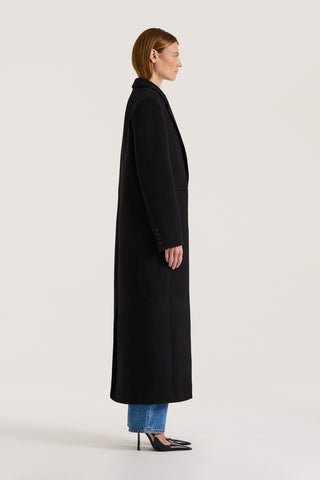 Side view of a model wearing a long black coat on a white background