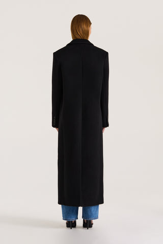 Back view of a model wearing a long black coat on a white background