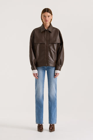 Model wearing a chocolate leather-effect jacket and blue jeans against a white background.