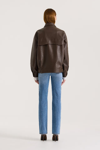 Back view of a model wearing a chocolate leather-effect jacket and blue jeans against a white background.