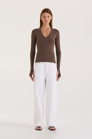Model wearing a chocolate long sleeve top and white wide leg jeans on a white background