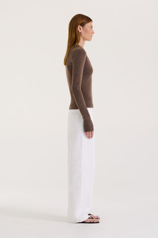 Side view of a model wearing a chocolate long sleeve top and white wide leg jeans on a white background