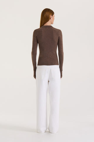 Back view of a model wearing a chocolate long sleeve top and white wide leg jeans on a white background