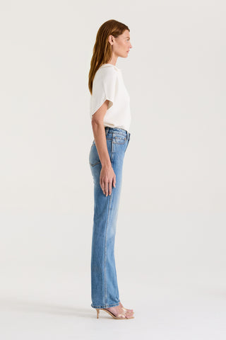 Side view of a model wearing a white loose fitting t-shirt and blue high rise, straight leg jeans on a white background