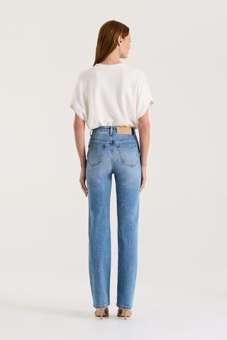 Back view of a model wearing a white loose fitting t-shirt and blue high rise, straight leg jeans on a white background