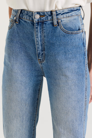 Close up view of a model wearing blue high rise, straight leg jeans on a white background