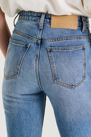 Close up back view of model wearing light blue high rise denim jeans with a Henne leather patch on a white background
