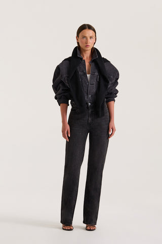 Petite model wearing a black denim jacket and Black slim fitted jeans on a white background
