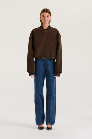 Model wearing a chocolate suede effect jacket and blue jeans on a white background