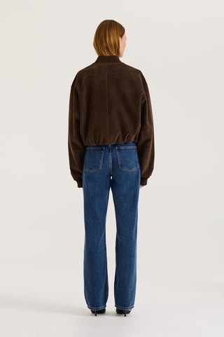 Back view of a model wearing a chocolate suede effect jacket and blue jeans on a white background