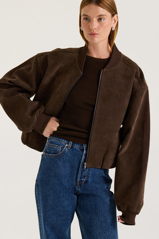 Model wearing a chocolate suede effect jacket and blue jeans on a white background