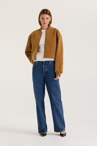 Model wearing a tan suede effect jacket with a white tank top underneath and indigo jeans on a white background