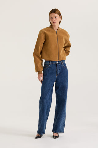 Model wearing a tan suede effect jacket and indigo jeans on a white background