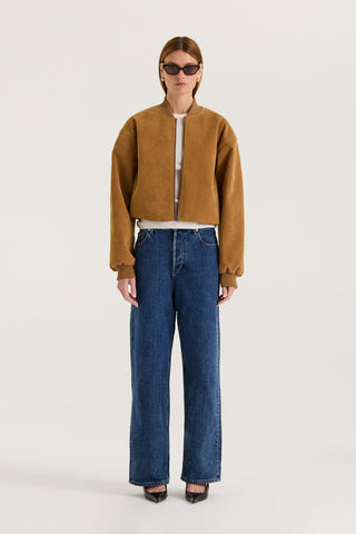 Model wearing a tan suede effect jacket and indigo jeans on a white background