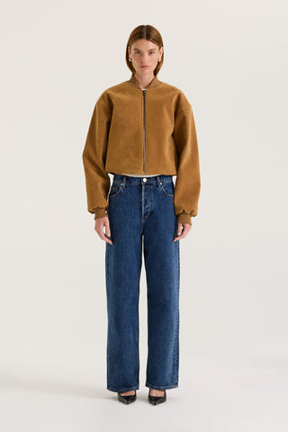 Model wearing a tan suede effect jacket and indigo jeans on a white background