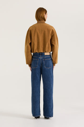 Back view of a model wearing a tan suede effect jacket and indigo jeans on a white background