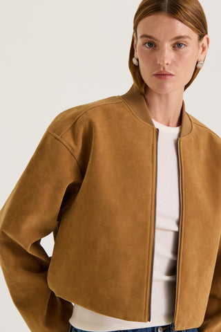 Model wearing a tan suede effect jacket with a white tank top underneath on a white background