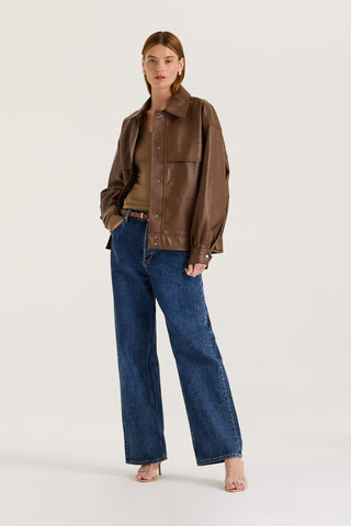 Model wearing a brown leather effect jacket and blue jeans on a white background