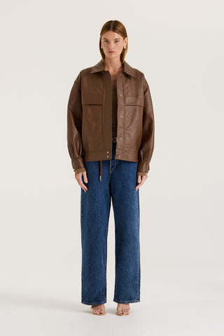 Model wearing a brown leather effect jacket and blue jeans on a white background