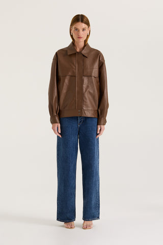 Model wearing a brown leather effect jacket and blue jeans on a white background