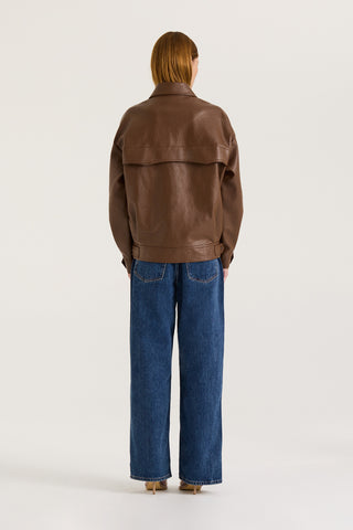 Back view of a model wearing a brown leather effect jacket and blue jeans on a white background