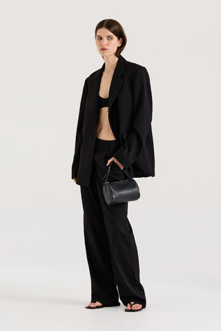 Model wearing a black Blazer with matching black pants holding a black handbag on a white background
