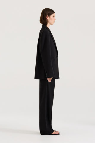 Side view of a model wearing a black Blazer with matching black pants on a white background