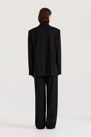 Back view of a model wearing a black Blazer with matching black pants on a white background