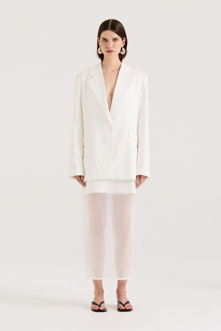 Model wearing a white blazer and a white skirt on a white background