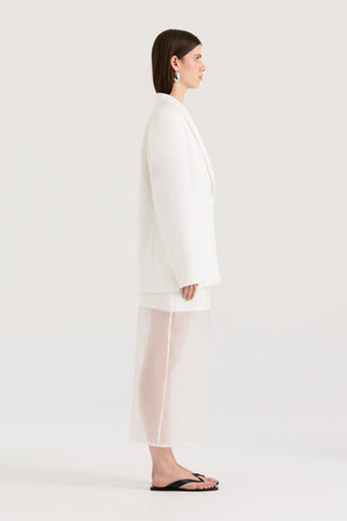 Side view of a model wearing a white blazer and a white skirt on a white background