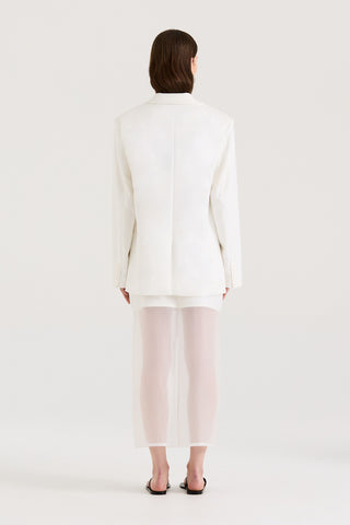 Back view of a model wearing a white blazer and a white skirt on a white background