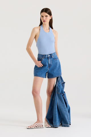 Model wearing a light blue halter top and indigo denim shorts, holding a denim jacket against a white background.