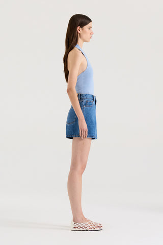 Side view of a model wearing a light blue halter top and indigo denim shorts on a white background.