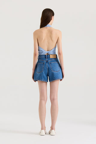 Back view of a model wearing a twist-back halter top and indigo denim shorts against a white background.