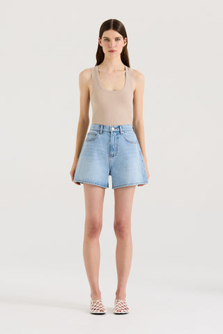 Model wearing a beige tank top and light blue denim shorts on a white background