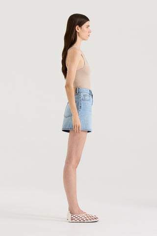 Side view of a model wearing a beige tank top and light blue denim shorts on a white background