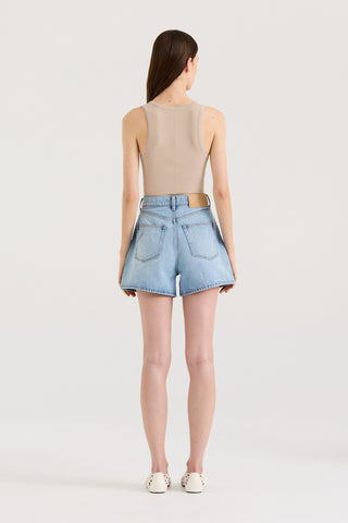 Back view of a model wearing a beige tank top and light blue denim shorts on a white background