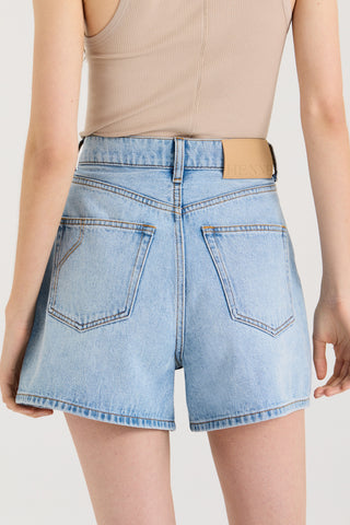 Close up back view of model wearing light blue denim shorts with a Henne leather patch on a white background
