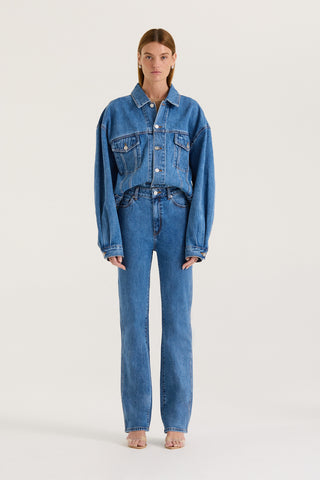 Model wearing an indigo denim jacket and indigo wash high rise, straight leg jeans on a white background