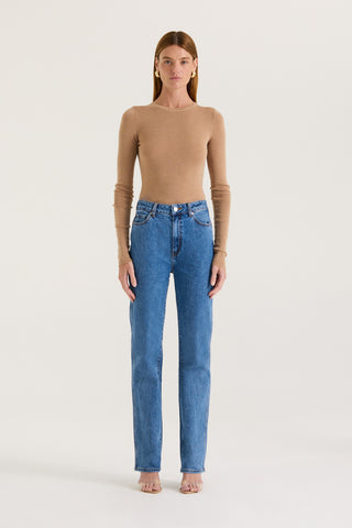 Model wearing indigo straight leg, high rise jeans and a tanned long sleeve top on a white background