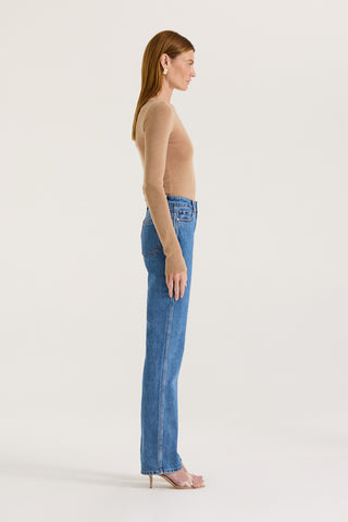Side view of a model wearing indigo straight leg, high rise jeans and a tanned long sleeve top on a white background