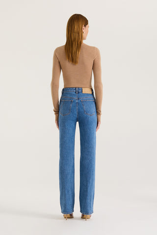 Back view of a model wearing indigo straight leg, high rise jeans and a tanned long sleeve top on a white background